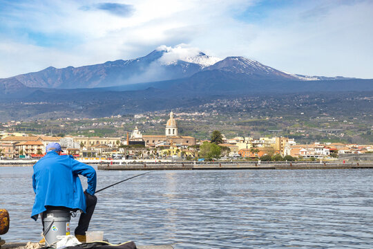 Riposto vista dal porto marinaro con pescatore in primo piano e con il vulcano Etna sullo sfondo - Sicilia