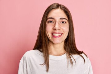 Fototapeta premium Portrait of happy, smiling, young girl in casual white t-shirt posing against pink studio background. Feeling good. Positive mood. Concept of youth, emotions, facial expression, lifestyle