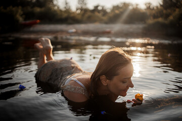Beautiful young woman in lake water in summer dress at sunset. Portrait of a romantic wet girl at...