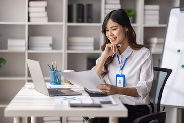 Charming Young asian businesswoman sitting on laptop computer in the office,           asian employee business making report calculating balance Internal Revenue Service checking document.