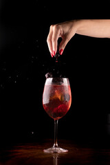 sexy female hand finishing refreshing cocktail with berries on dark background and wooden table