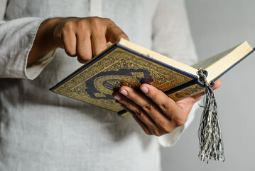 Holy Quran in Hand with arabic calligraphy meaning of Al Quran. Muslim man pointing the finger on...