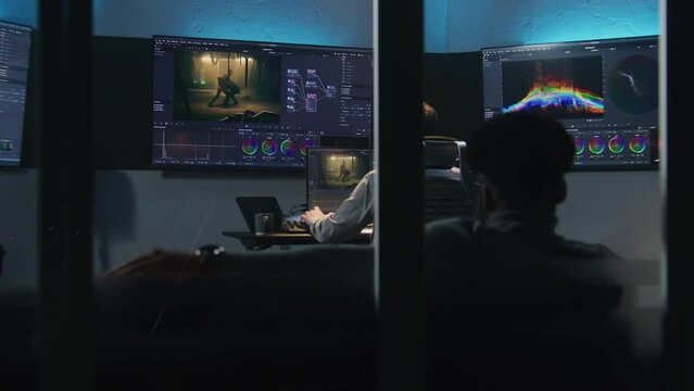 Multi ethnic colorist and film maker edit movie and make color grading in professional software. Process of colour correction for video post production in studio. Screens with action film footage.