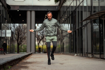 A middle-aged man is skipping a jumping rope outside in an urban area.