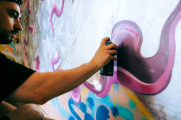 Young caucasian man graffiti artist drawing on a wall.
