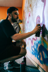 Young caucasian man graffiti artist drawing on a wall.