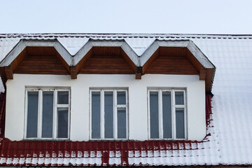 Snow on the roof of a red, brown metal roof of a European house with a window