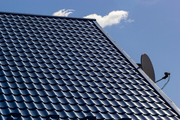 The roof of a house covered with sheets of blue metal tiles against the background of the sky on a summer day. Business selling building materials or repairing house roofs