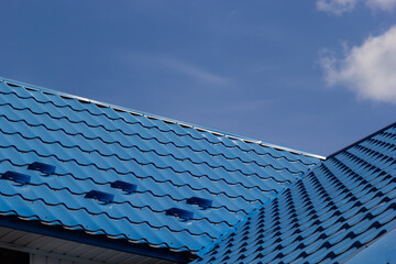 The roof of a house covered with sheets of blue metal tiles against the background of the sky on a summer day. Business selling building materials or repairing house roofs