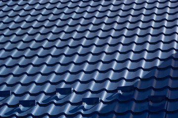 The roof of a house covered with sheets of blue metal tiles against the background of the sky on a summer day. Business selling building materials or repairing house roofs