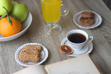 Obraz na płótnie Canvas Cup of tea, plates with cookies, glass of orange juice, books, reading glasses, bowl of fruit and candles on the table. Selective focus.