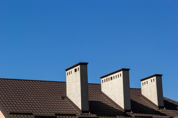 Obraz premium Roof of a new home. Ceramic chimney, metal roof tiles, gutters, roof window. Single family house