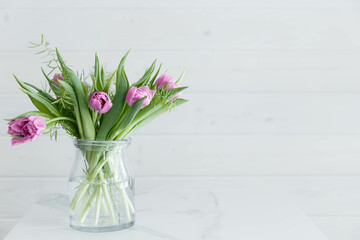 Purple bouquet of tulips on a marble table against a white wooden wall.