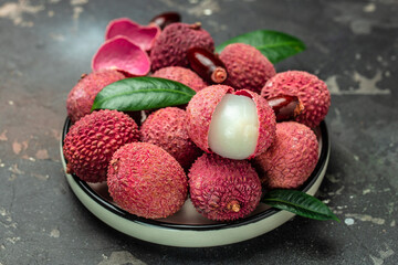Juicy Lychee with cut in half and leaves on plate on a dark background, top view