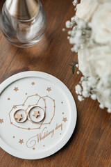 golden wedding rings lie on a white wedding tray next to a bouquet of flowers and a bottle of perfume on a wooden background