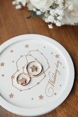 gold wedding rings lie on a white wedding tray next to a bouquet of flowers on a wooden background