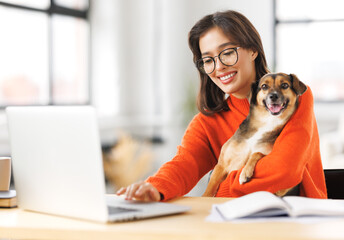 happy woman freelancer working on laptop remotely from home together with pet dog