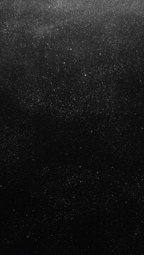 Vertical video. Dust floating. Night snow. Galaxy stardust storm. Grain texture overlay. Silver white shiny glitter particles floating on dark black abstract background.