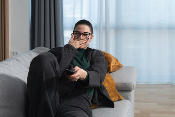 Young business woman day off relaxing on the couch, using remote control and choosing a TV show or movie on the television menu. Free female spending alone day at home, weekend activity concept