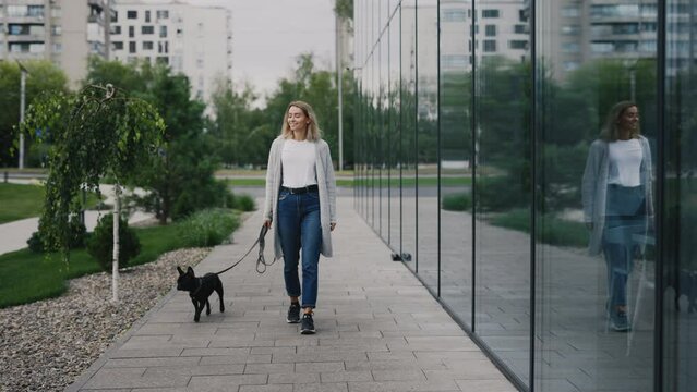 Caucasian Woman on a Walk with a Small Black French Bulldog and Training Him. Female Walks a Dog near the House and Exercising with Her Puppy. People and Dogs Friendship Concept
