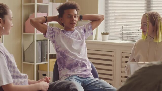 Medium slowmo of happy Biracial teen boy speaking to psychology specialist at group therapy session while sitting in circle with other teenagers listening to him