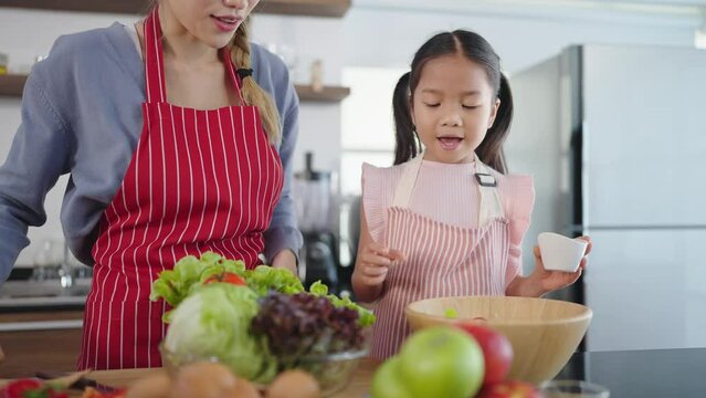 Happy Asian family mother teaching lovely daughter to cooking vegetable salad in kitchen room at home. Healthy meal and dinner, happy family asian concept