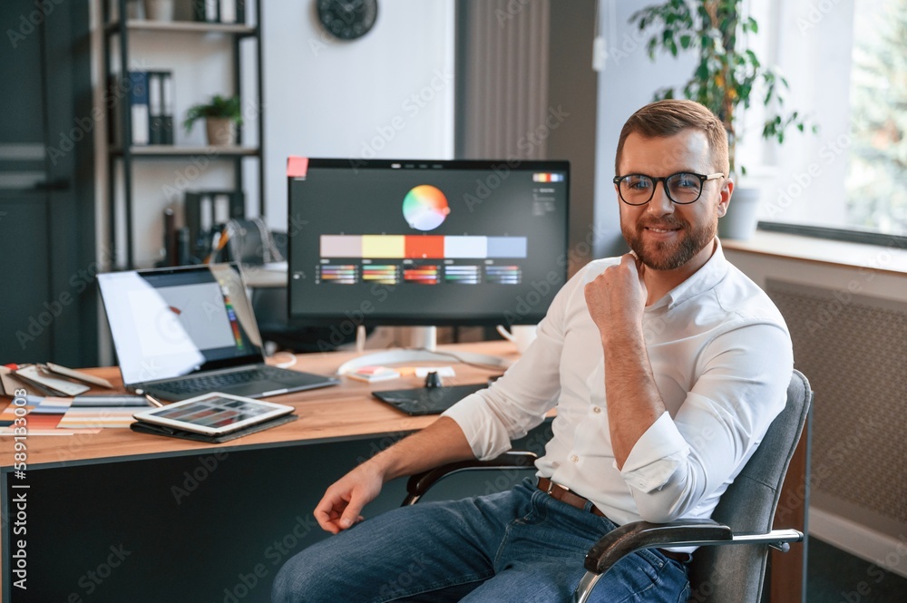 Poster sitting and smiling. man in formal clothes is working in the modern office. using computer