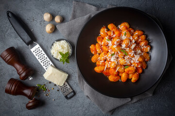 Traditional Italian food potato gnocchi with tomato sauce, parmesan cheese and fresh basil on dark table. Top view. Healthy food.