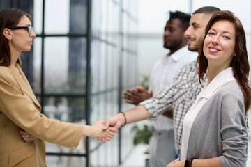 ambitious business woman smiling at the camera against the backdrop of a meeting of colleagues