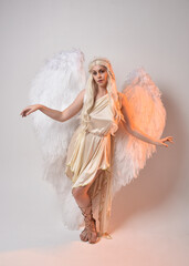 Full length portrait of beautiful blonde woman wearing a fantasy goddess toga costume with feathered angel wings. 
 Jumping pose like flying, isolated on white studio background.