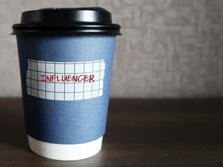 Blue coffee cup with sticker label INFLUENCER, refer to one who has power to affect purchase decisions of others because of their authority, knowledge, position or relationship