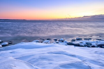 Scenic view of a beautiful sunrise with a snow-covered beach next to the water
