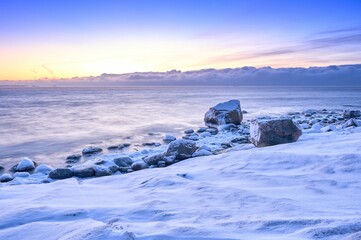 Obraz premium Scenic view of a beautiful sunrise with a snow-covered beach next to the water