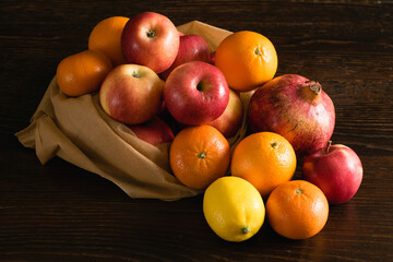Fruit in a reusable bag. Earth day and zero waste concept. Apples, lemon, oranges and pomegranate on a dark wooden background.