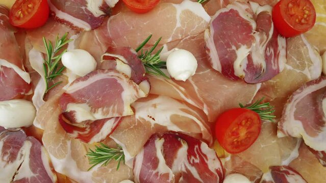 Slices of raw ham, view from top. Italian cured pork meat with mozzarella, tomatoes, and fresh rosemary