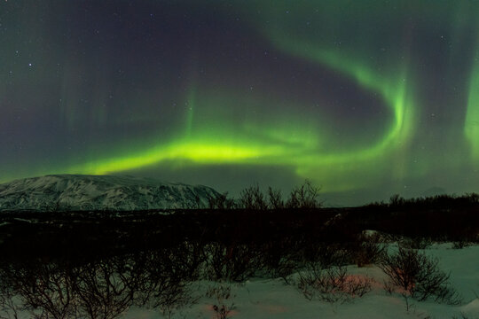 imagen de un paisaje nocturno nevado, con montañas de fondo, y una aurora boreal sobre el cielo de Islandia 
