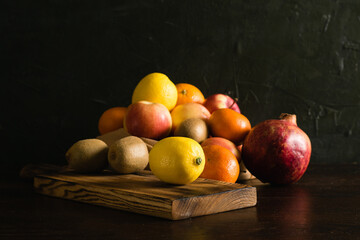 Fruit in a reusable bag. Earth day and zero waste concept. Orange, lemon, apple, kiwi, pomegranate and wooden cutting board on dark background