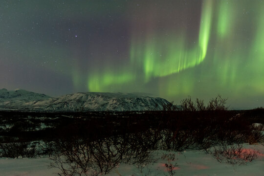 imagen de un paisaje nocturno nevado con montañas al fondo y una aurora boreal en el cielo de Islandia 