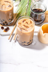 Iced tapioca coffee latte or boba pearl bubbles milk tea, asian trendy cold coffee drink with tapioca balls and crushed ice, on white marble background copy space
