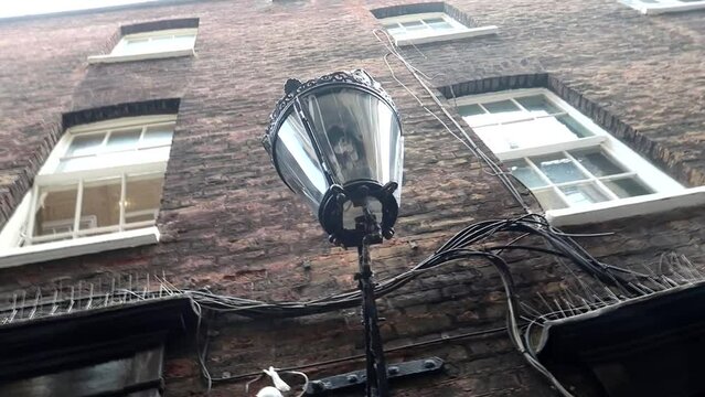Black street lamp on a dirty brick wall of a building. Goodwin's Court, London