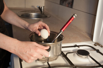 A girl boils egg in a metal pan on a white gas stove in the kitchen. Image for your creative decoration or design.