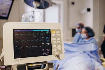 Medical researcher examining EKG image showing on monitor while patinet with mask running on cross trainer testing heart rate using electrodes.