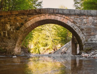 Fototapeta na wymiar an arched stone bridge spans a river beneath a wooded forest
