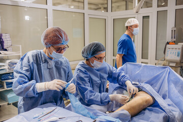 Surgeons operate on the legs of an elderly woman with varicose veins.