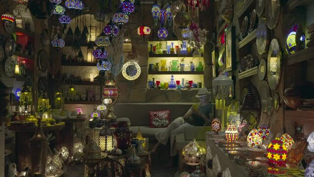 Adult woman sits in an Arabic-style Middle Eastern cafe and looks at mobile phone. Near Eastern cafe interior with multicolored lamps in semi-darkness