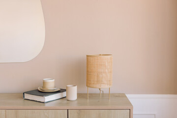 Rattan lamp, ceramics, book on wood console in living room. Copy space. Mockup wall.