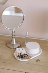 A table mirror, ceramics for storing jewelry, a perfume bottle on a bedside wooden table.