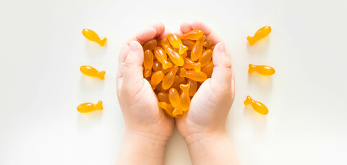 Child hands holding fish oil capsules on white background. Omega 3, fish fat capsules in kid's hands. Children's health care concept. Banner.