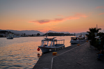 Beautiful colorful sunset on the seashore with taxi ferry boats. Poros Island, Greece.