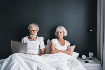 Senior woman angry at her husband using laptop computer working at bed.